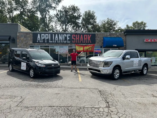 Appliance Shark appliance store exterior with delivery vehicles parked outside and a “Now Open” banner, offering discounted scratch-and-dent appliances in Kansas City.